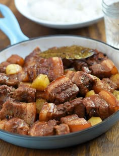 meat and potatoes in a pan on a wooden table next to a glass of water