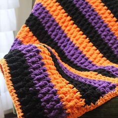 an orange and purple crocheted blanket sitting on top of a chair