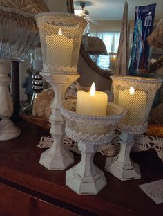 three white candles sitting on top of a table next to a mirror and other items