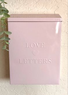 a pink box with the words love and letters on it next to a green plant