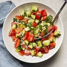 a white bowl filled with cucumber and tomato salad on top of a table