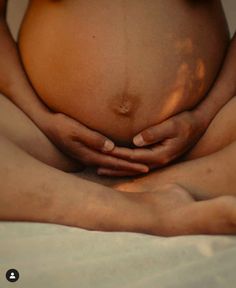 a pregnant woman is holding her hands on her belly while sitting in the middle of her stomach