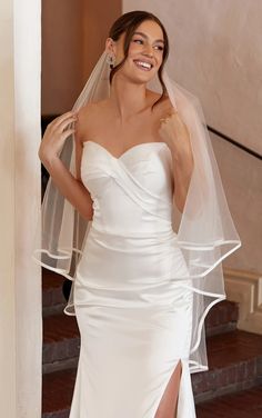 a woman in a white wedding dress is posing for the camera with her veil over her head