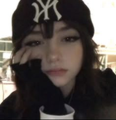 a woman wearing a new york yankees hat and black jacket with her hand on her face