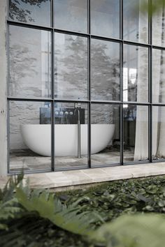 a bath tub sitting inside of a window next to a lush green plant covered ground