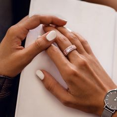 a woman's hands with two rings and a watch on top of a book