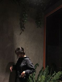 a woman standing in front of a window next to a plant