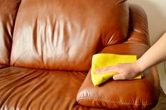 a person cleaning a brown leather couch with a yellow micro towel