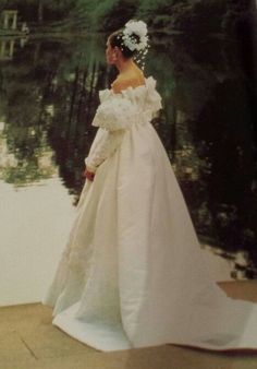 an old photo of a woman in a wedding dress standing next to a body of water