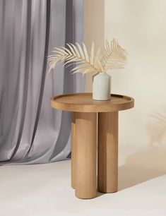 a round wooden table with a plant on it in front of a curtained window