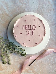 a cake with the word hello 23 on it next to a pink ribbon and flowers