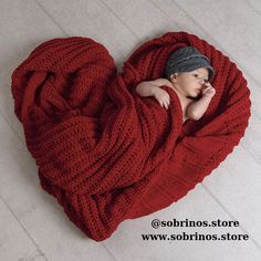 a baby wrapped in a red blanket is laying on the floor with his head resting on his hand