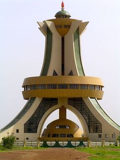 a tall building with a clock on the top of it's face in front of a green field