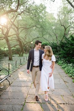 a man and woman walking down a path in the park at sunset, holding hands