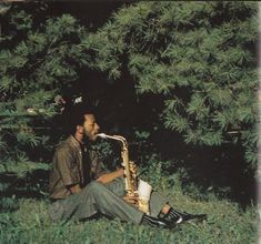 a man sitting in the grass playing a saxophone