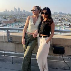 two women standing next to each other on top of a building