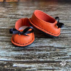 an orange pair of baby shoes sitting on top of a wooden table with black ribbon