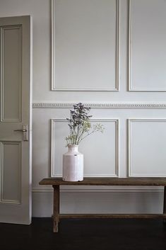 a white vase sitting on top of a wooden bench next to a wall with paneling