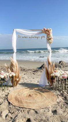 an outdoor wedding setup on the beach with flowers and pamoits in front of it