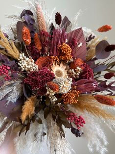 an arrangement of dried flowers and feathers in a vase