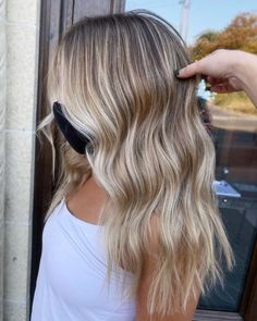 a woman with long blonde hair is combing her wavy, light - blonde hair