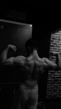 a man flexing his muscles in front of a brick wall