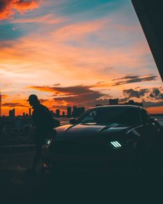 a man standing next to a car in front of a sunset