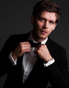 a man in a tuxedo adjusts his bow tie while looking at the camera