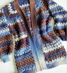 a crocheted sweater is laying on top of a white surface and it has blue, brown, and white stripes