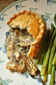 a piece of pie and asparagus on a blue and white plate with a fork