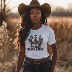 Dive into the essence of Western elegance with our 'Black Rodeo Unisex Tee,' a fashion statement that celebrates heritage and the adventurous spirit of three stunning Black women on their majestic rides. Perfect for individuals passionate about Western equestrian culture, heartland melodies, and the vibrant traditions of rodeo, this tee is a tribute to the enduring strength of cowgirl legends. Crafted from premium soft materials for ultimate comfort and durability, it's ideal for any setting, from country outings to casual gatherings. Offering a range of sizes to ensure a perfect fit for everyone, this versatile tee bridges modern fashion with traditional homage, making it a must-have for those who cherish the legacy of Black cowgirls and the timeless charm of Western culture, all while em Cattle Barons Ball Outfit, Women Cowboy Outfits, Cowgirl Outfits Black Women Rodeo, Country Outfit Black Women, Rodeo Outfits For Women Black, Band Merch Tops With Custom Print, Fitted Band Merch Shirt, Black Cowgirl Outfits For Women, Cali Cowgirl