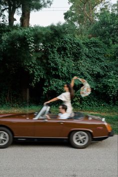 two people are riding in the back of a convertible car and one person is holding up a frisbee