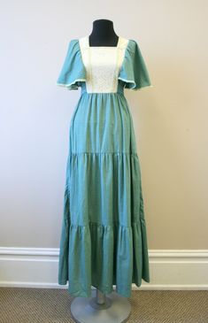 "Description: Vintage 1970s green and cream prairie style maxi dress. Polyester/cotton blend. It has a square neckline, with a lace covered bodice. It has crocheted trim. Short, fluttery sleeves and a ruffled hem. It has attached back ties. Tiered style skirt. Condition: In good condition. No holes. It has a few faint spots. The trim on this dress is very faintly green -- the color bled when it was soaked and attached to the crochet trim. But it is completely even all around, and looks intention Green Maxi Dress With Lace Trim For Spring, Spring Maxi Dress With Lace Trim And Square Neck, Fitted Peasant Maxi Dress With Ruffles, Spring Prairie Dress With Lace Trim Maxi Length, Cotton Maxi Dress With Lace Trim For Garden Party, Vintage Green Cotton Maxi Dress, Vintage Cotton Maxi Dress With Lace Trim, Green Vintage Cotton Maxi Dress, Cotton Prairie Dress With Lace Trim For Summer