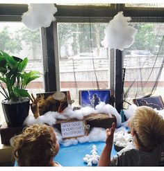 two children are sitting at a table with fake clouds and pictures on the window sill