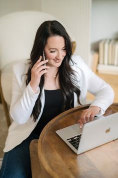 a woman sitting at a table talking on her cell phone while using a laptop computer