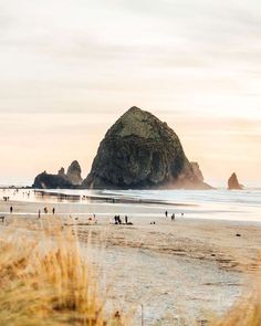 people are walking on the beach near some rocks