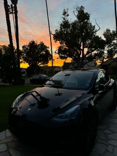 a black car parked on the side of a road next to palm trees at sunset