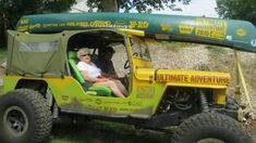 a man sitting in the driver's seat of a green and yellow jeep with an awning