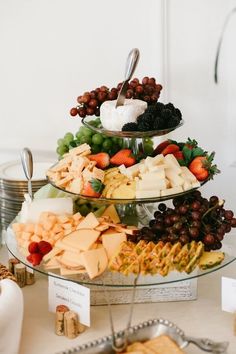 three tiered platter filled with cheese, fruit and crackers on a table