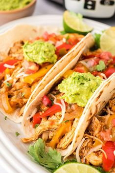 three chicken tacos on a plate with guacamole and lime wedges