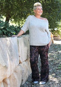 a woman standing next to a stone wall with her hands on her hips and smiling