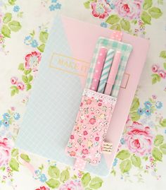 three pink and blue pens sitting on top of a notepad next to a notebook