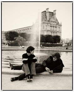 two people sitting on the ground in front of a fountain