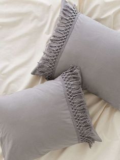 two gray pillows with ruffled edges on top of a white sheeted comforter