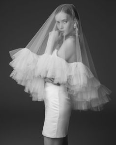 black and white photo of woman in wedding dress with veil over her head, posing for the camera