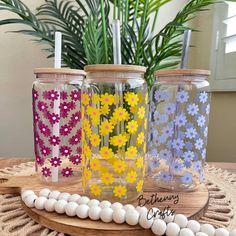 three mason jars with flowers painted on them sitting on a table next to white balls