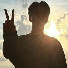 a man making the peace sign with his fingers in front of the sun behind him