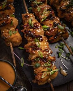 chicken skewers with sauce and garnishes on a slate platter