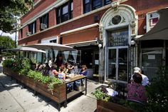 people sitting at tables in front of a building with umbrellas on the side walk