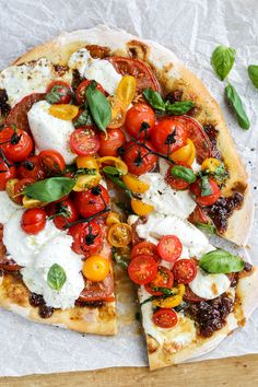 a pizza with tomatoes, mozzarella and basil on it sitting on a piece of parchment paper